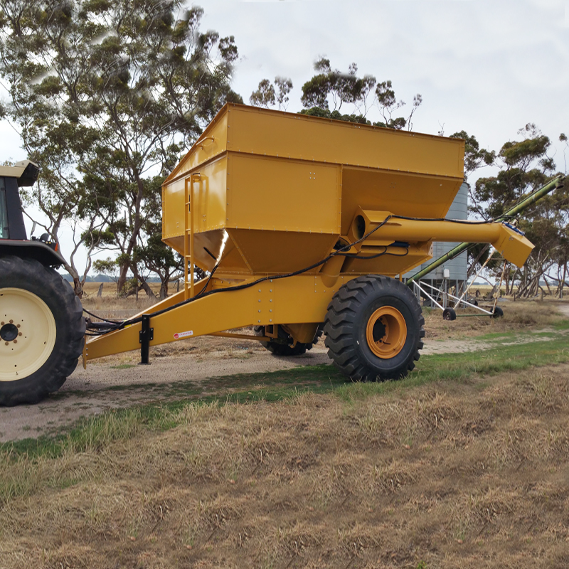 Yellow grain cart attached to a tractor in a rural field