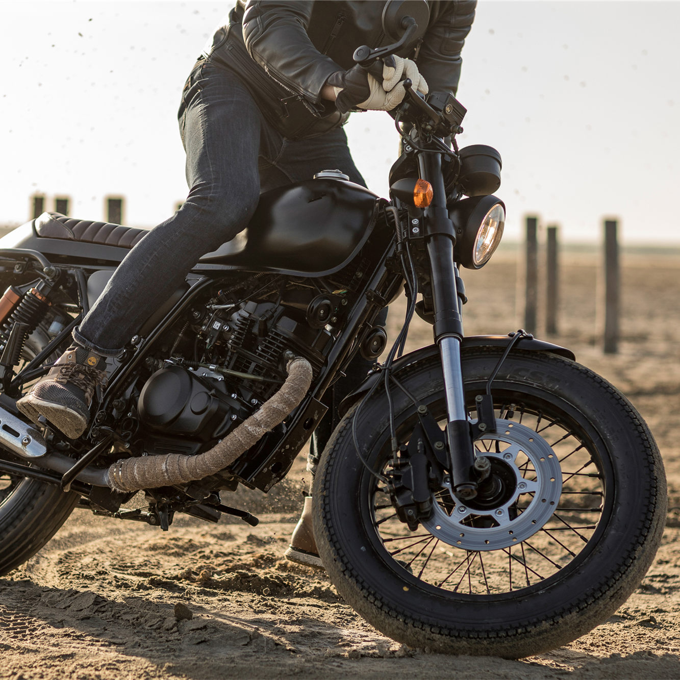 Retro style motorcycle being ridden on a sandy surface showing cafe racer aesthetic